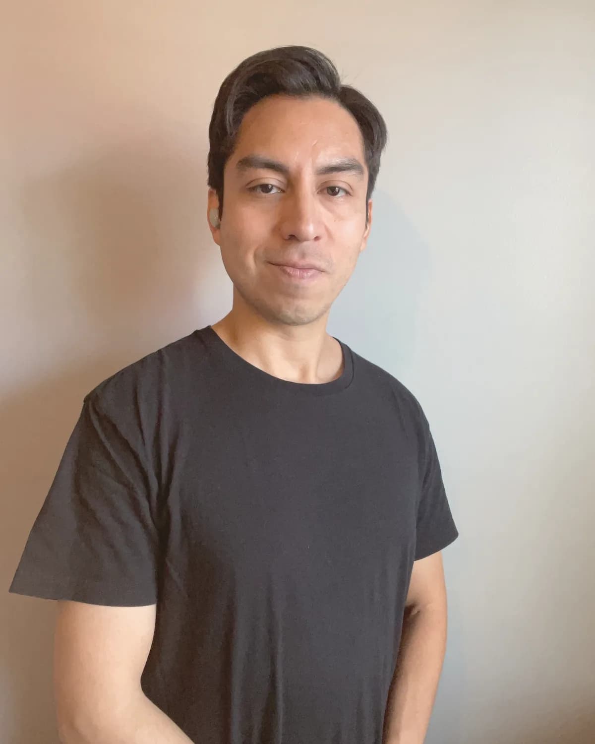 Scott Salvatierra in a black t-shirt against a cream wall.